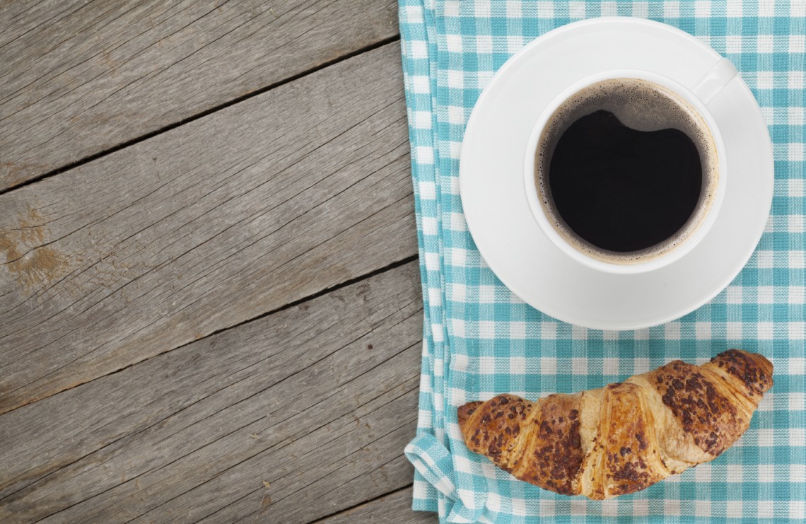 Cup of coffee and fresh croissant on wooden table with copy space